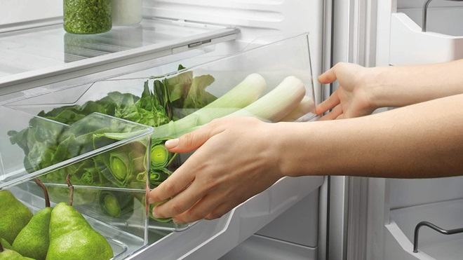 person taking green vegetables out of a fridge crisper